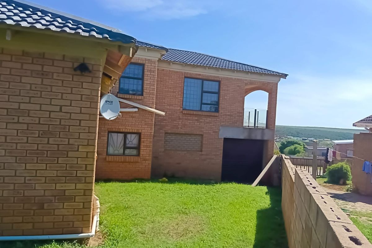 Rear view of a double-story face brick house featuring a balcony, garage access, and a private garden area with boundary walling.