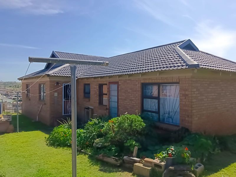 Rear view of a face brick house featuring a tiled roof, aluminium window frames, and security fixtures set within a garden area.