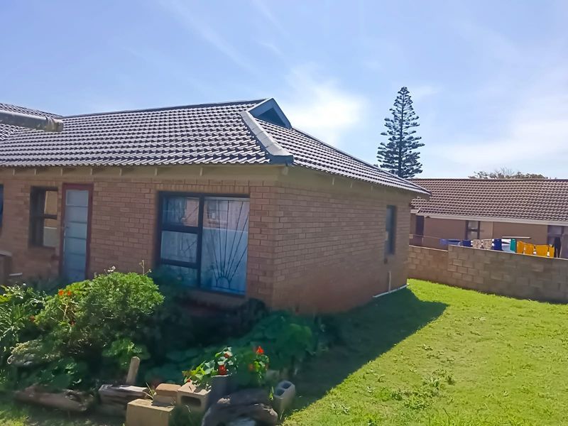 A view of the rear exterior of the brick house featuring a tiled roof, security bars on windows, and a surrounding garden area.