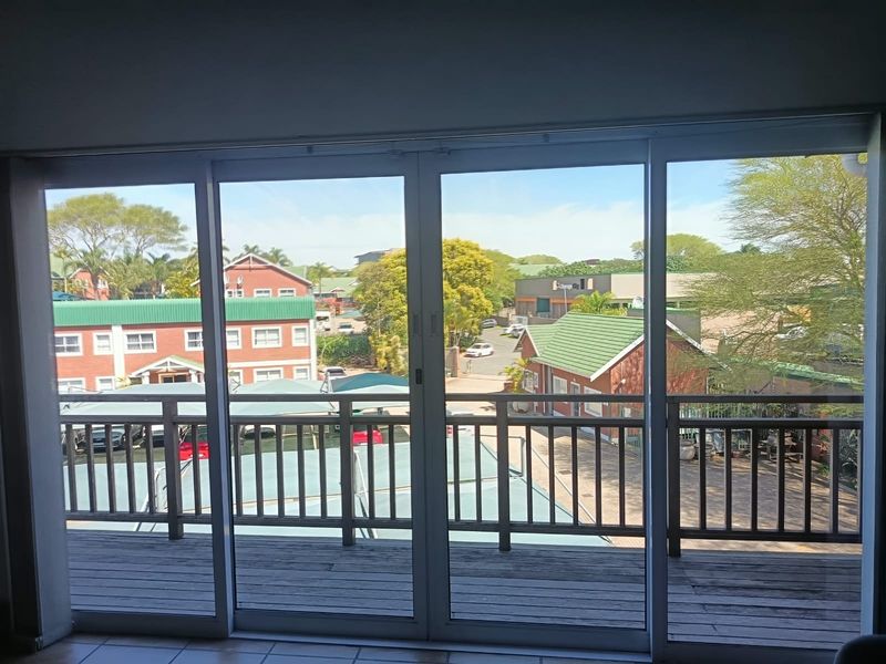 A view from an interior office space looking out through large sliding glass doors onto a wooden balcony overlooking the surrounding office park.