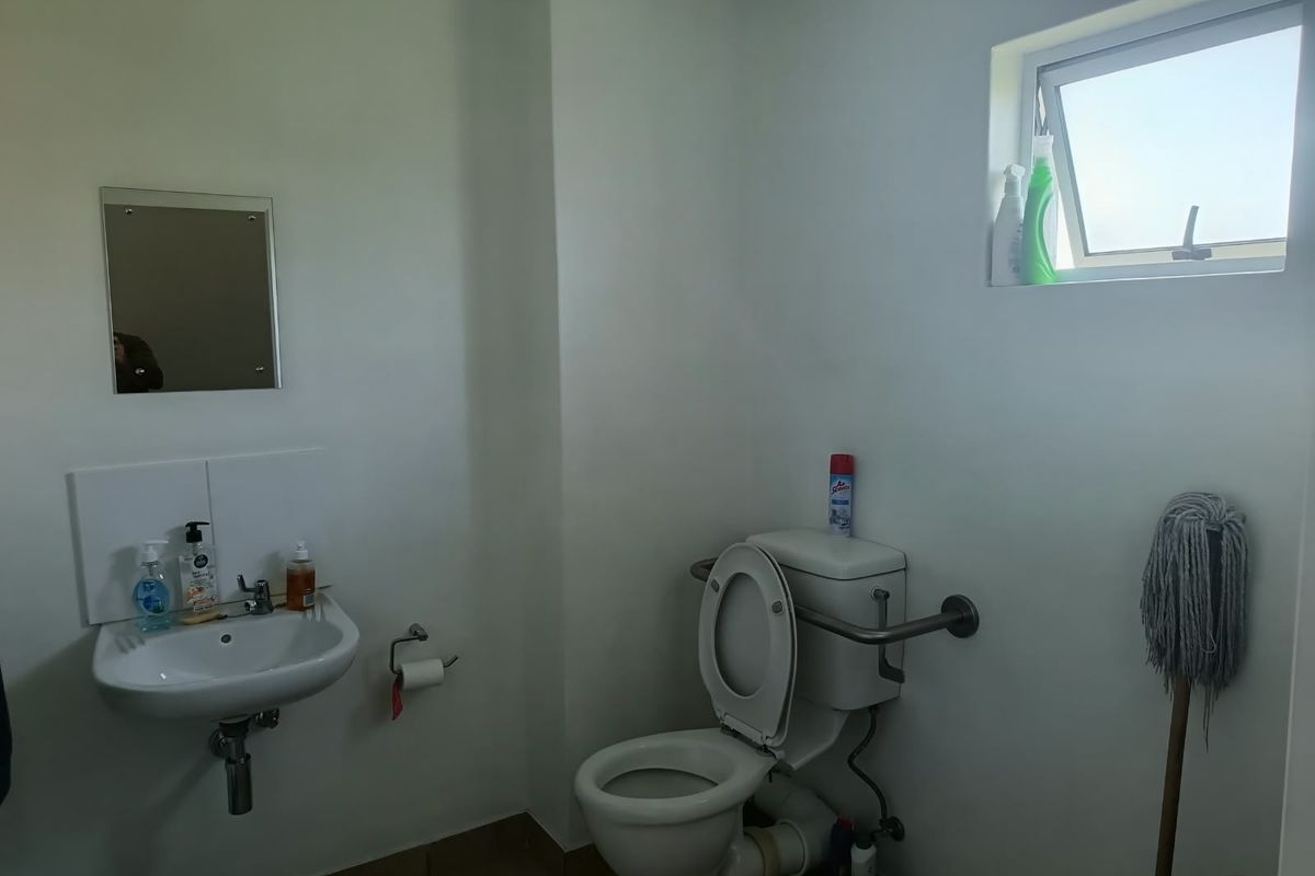 A functional office restroom featuring a wall-mounted basin, toilet with grab rail, and a small top-hung window for ventilation.