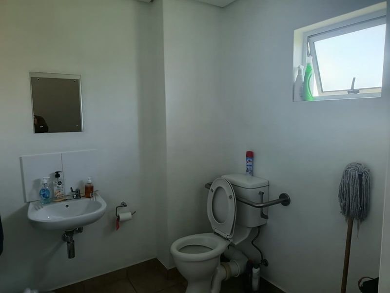 A functional office restroom featuring a wall-mounted basin, toilet with grab rail, and a small top-hung window for ventilation.