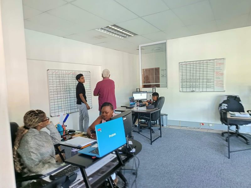 A functional office space featuring carpeted flooring, suspended ceilings with recessed lighting, and wall-mounted whiteboards, currently set up for collaborative work.