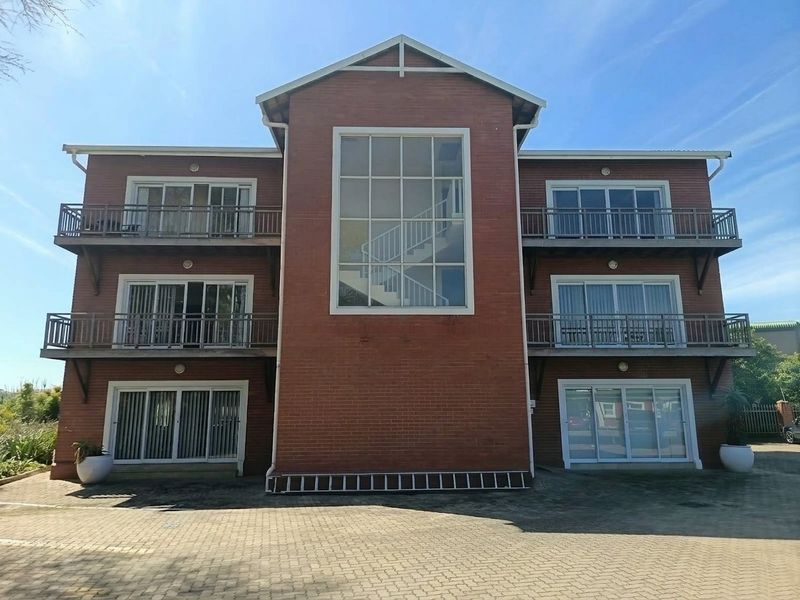 A three-story brick office building featuring multiple balconies, large sliding glass doors, and a prominent central window showcasing an internal staircase.