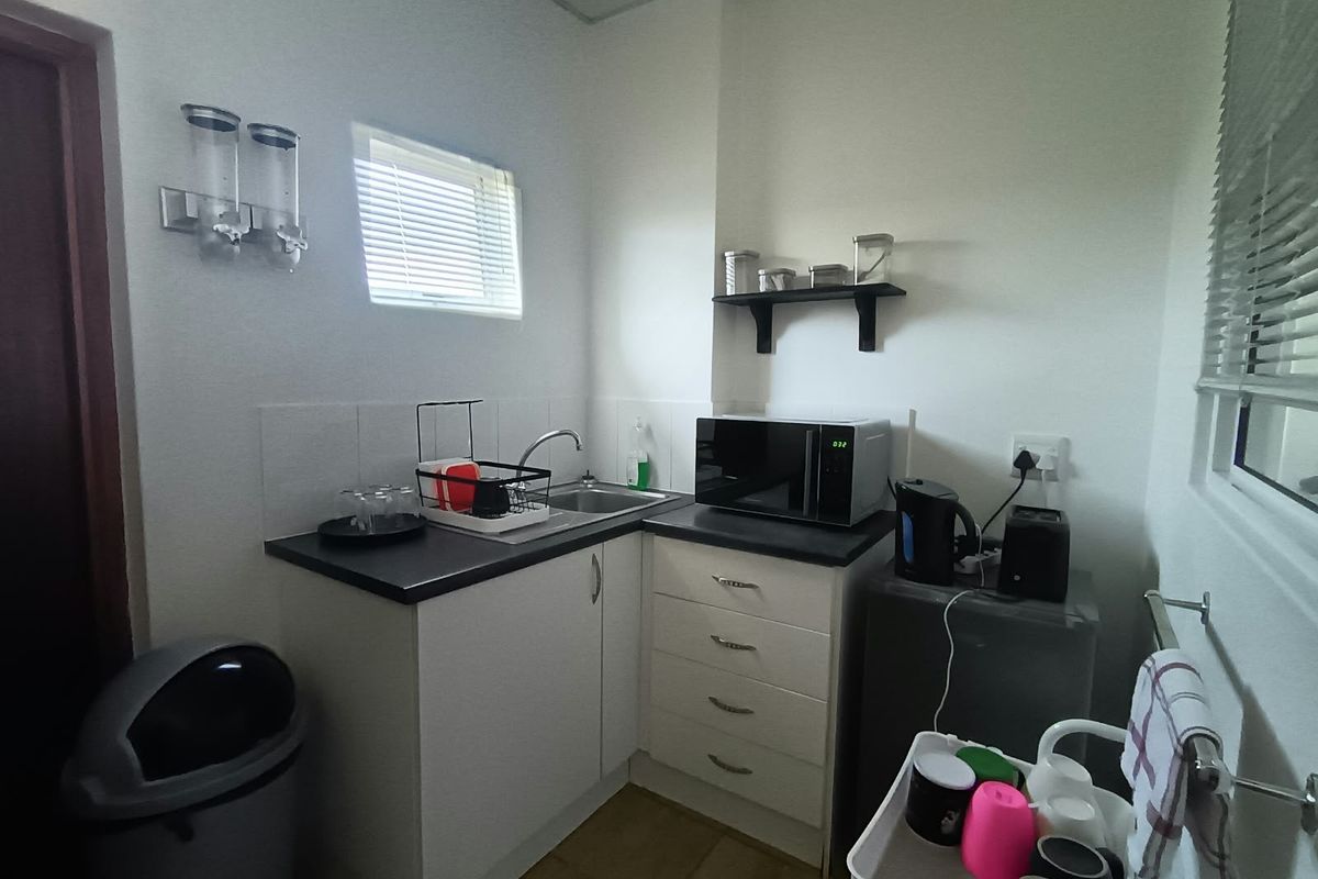 A compact office kitchenette featuring white cabinetry, a stainless steel sink, laminate countertops, and tiled splashbacks, providing essential utility for a workspace.