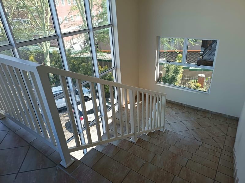 A bright, modern office stairwell featuring tiled flooring, a white metal balustrade, and large windows providing ample natural light.