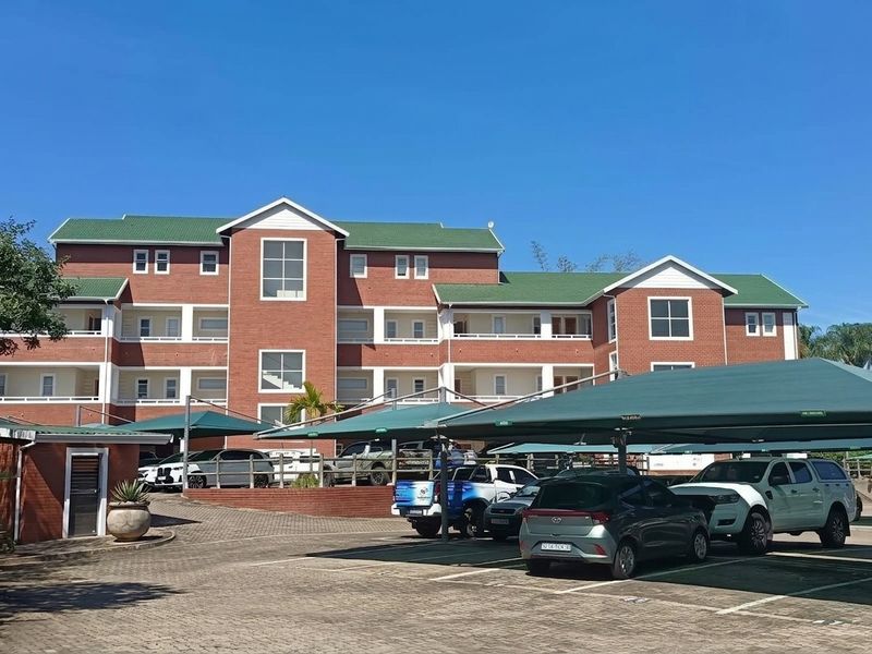 A multi-story office building featuring a red brick facade, green roof, and extensive covered parking facilities for staff and visitors.