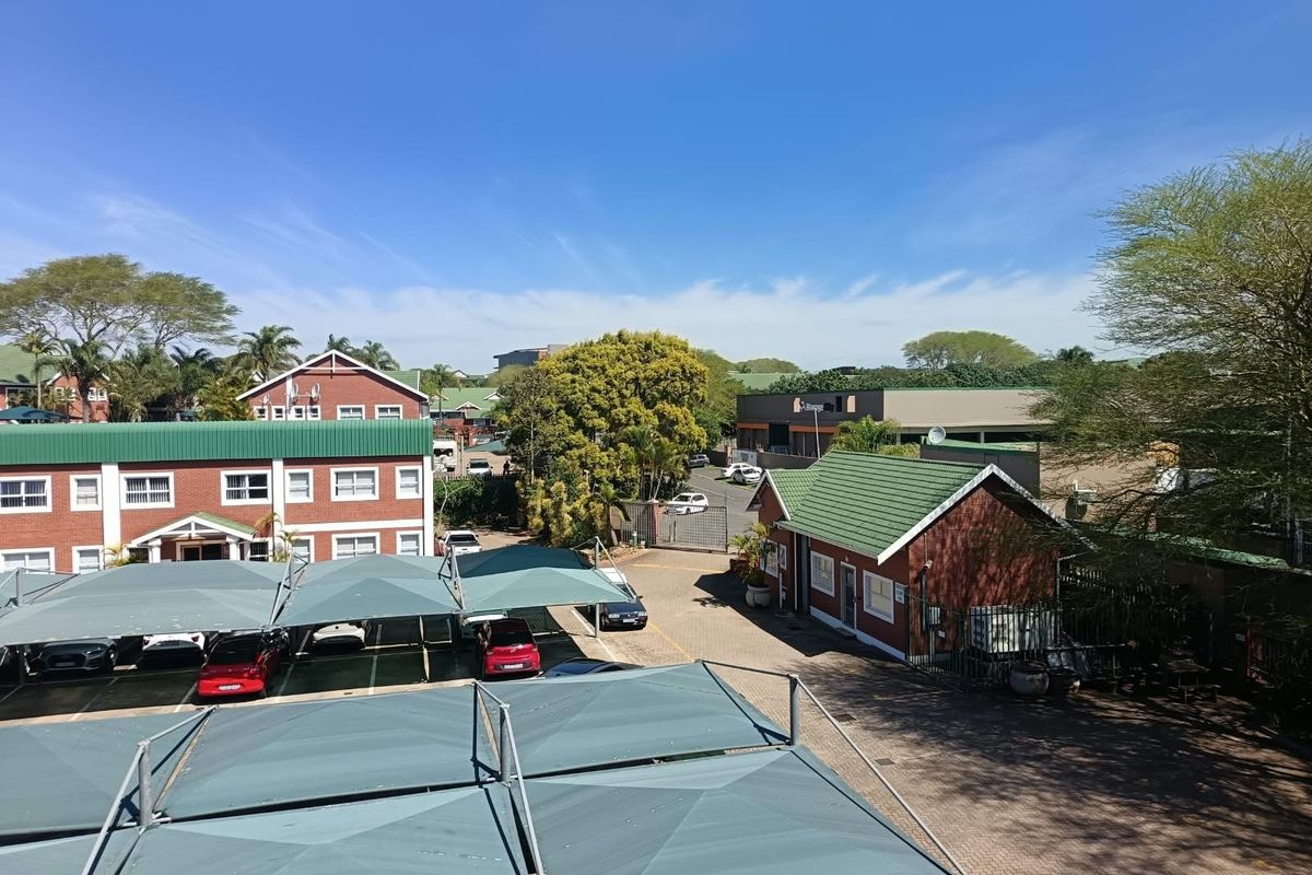 Aerial view of an office complex featuring brick buildings with green metal roofs, paved parking areas, and shade cloth carports.
