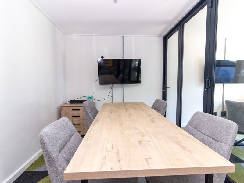 Modern office meeting room featuring a glass partition wall, exposed electrical conduit, and patterned carpet tiles.