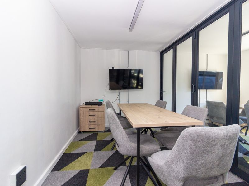 A modern office meeting room featuring glass partition walls, patterned carpet tiles, and a clean, professional aesthetic suitable for collaborative work.