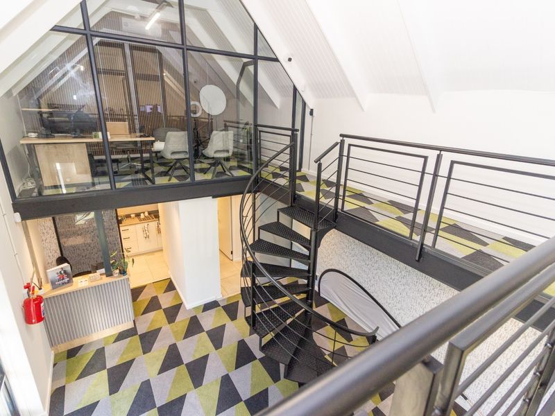 Modern office space featuring a mezzanine level with glass partitioning, a black spiral staircase, and contemporary patterned carpet flooring.