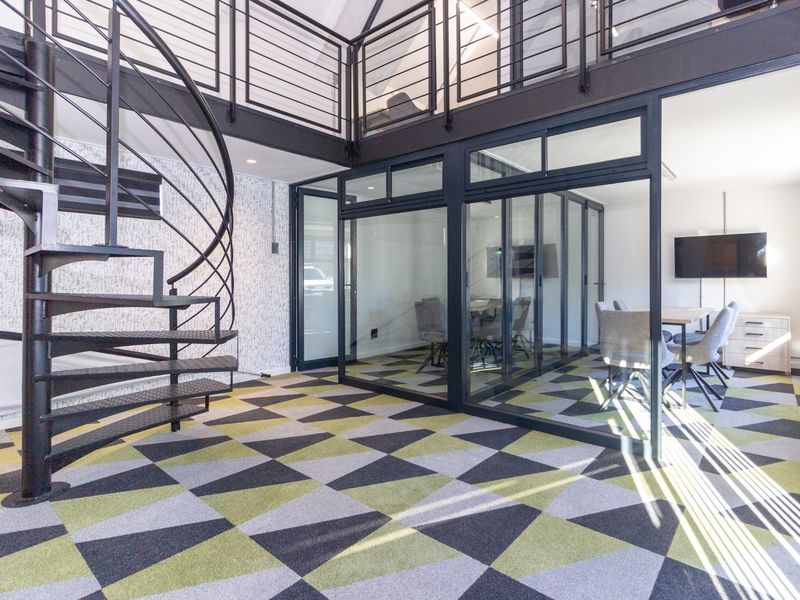 Modern office space featuring a striking spiral staircase, mezzanine level, and glass-partitioned meeting rooms with contemporary patterned carpeting.