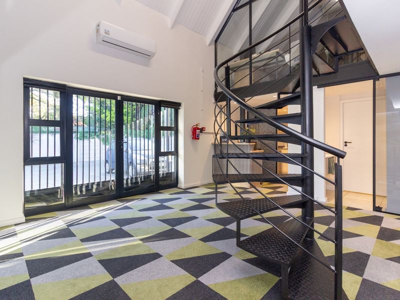 Modern office space featuring a striking black spiral staircase, mezzanine level, split-system air conditioning, and secure glass-paned entrance doors.