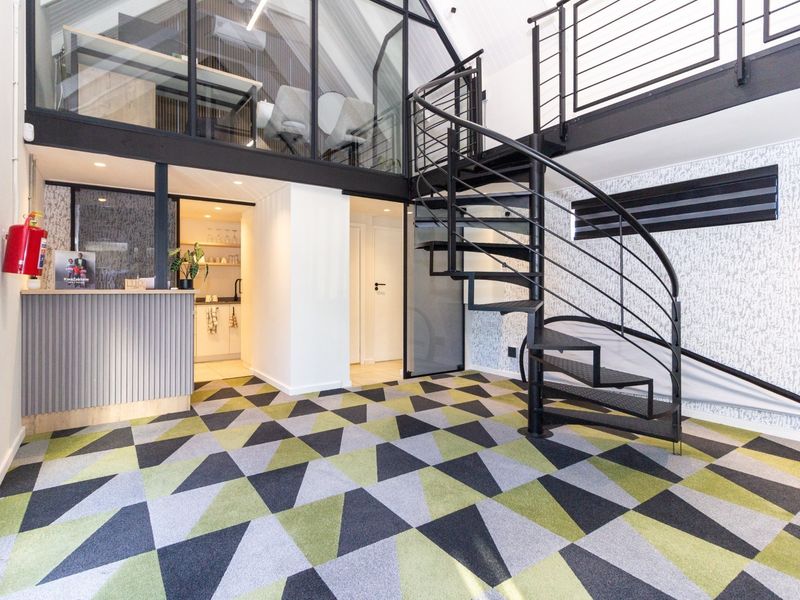 Modern office space featuring a striking spiral staircase, mezzanine level with glass partitioning, a reception area, and a compact kitchenette.