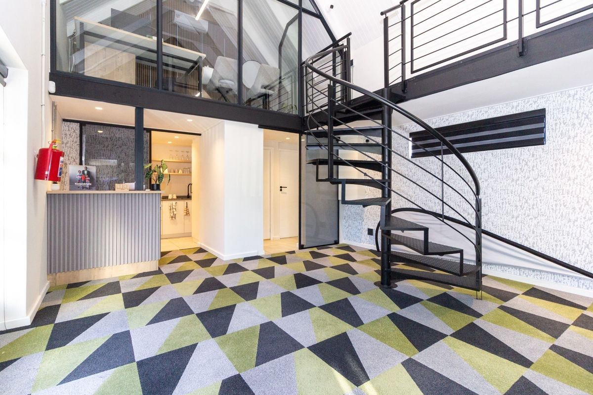 Modern office space featuring a striking spiral staircase, mezzanine level with glass partitioning, a reception area, and a compact kitchenette.