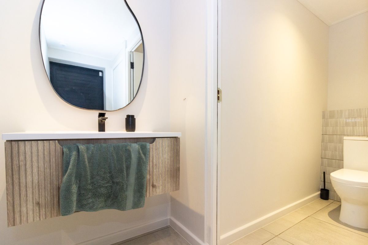Modern bathroom featuring a wall-mounted vanity with basin, contemporary faucet, and a clean toilet with tiled splashback and flooring.