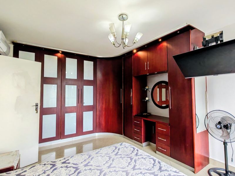 Bedroom featuring extensive dark wood built-in cabinetry with integrated vanity, tiled flooring, and wall-mounted air conditioning unit.