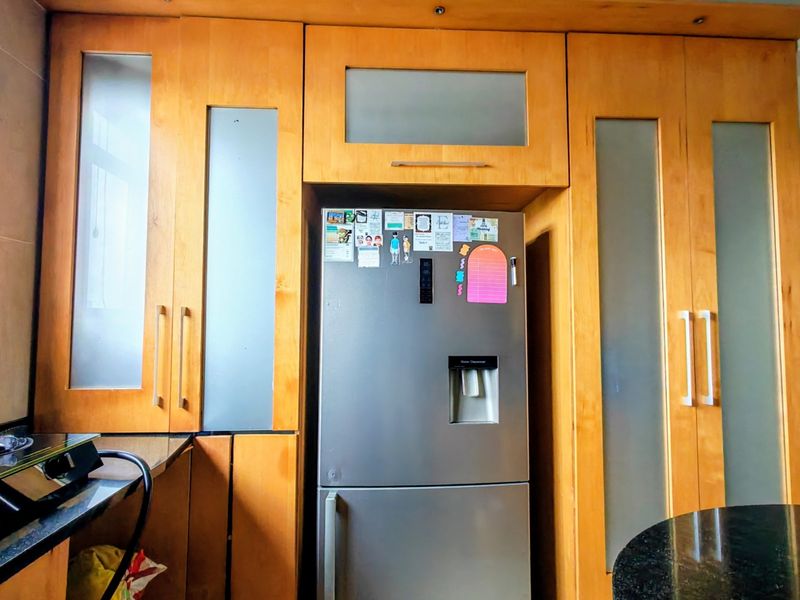 A kitchen area featuring light wood built-in cabinetry with frosted glass accents and dark granite countertops.