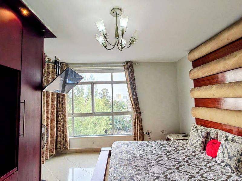 A bedroom featuring a large window with natural light, tiled flooring, and a built-in wardrobe.