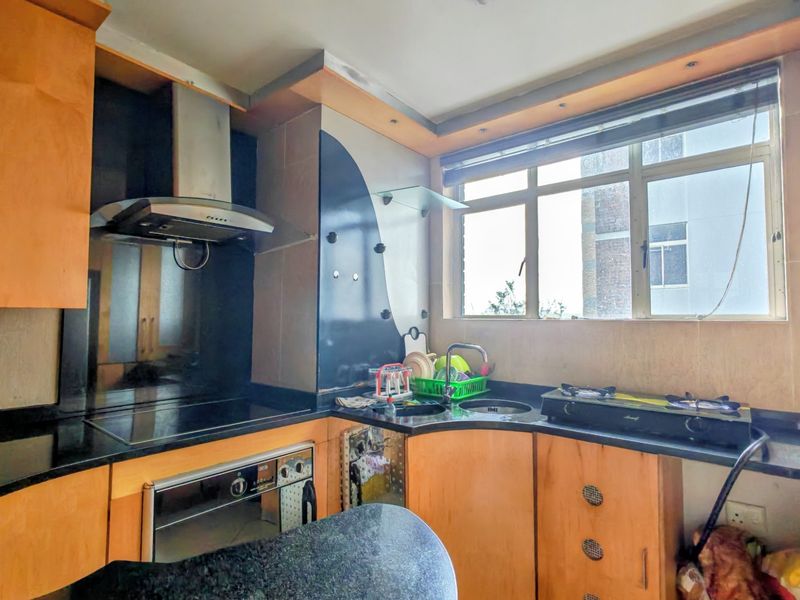 A compact kitchen featuring wooden cabinetry, black granite countertops, a built-in oven, and an extractor fan with a window for natural light.