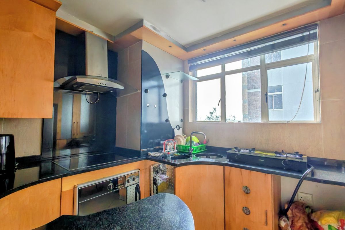 A compact kitchen featuring wooden cabinetry, black granite countertops, a built-in oven, and an extractor fan with a window for natural light.