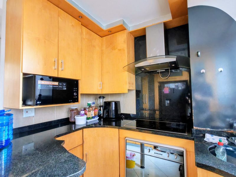 A functional kitchen featuring light wood cabinetry, dark granite countertops, a built-in oven, electric hob, and an integrated microwave.