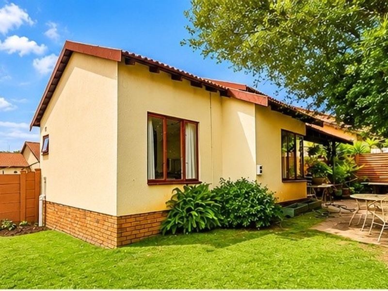 Rear view of the townhouse featuring a private garden, paved patio area, and established landscaping with timber-framed windows and a tiled roof.