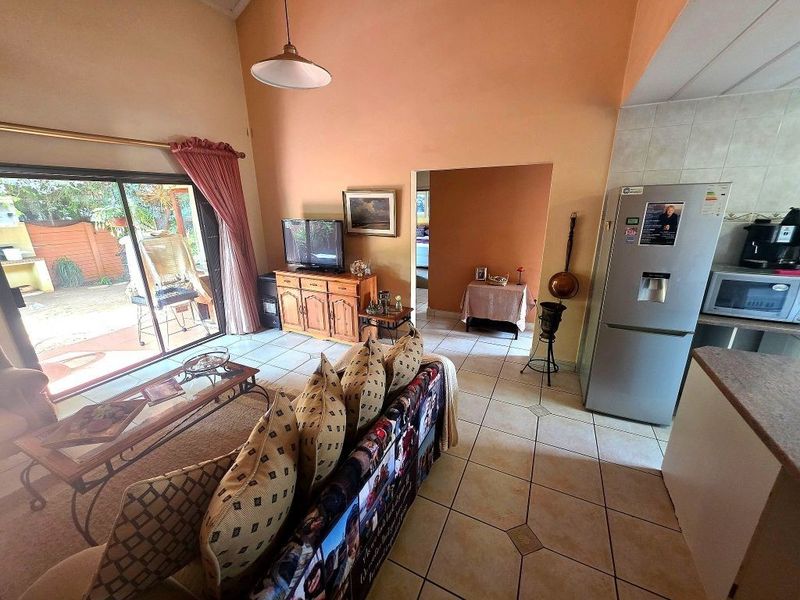 Open-plan living area featuring tiled flooring, vaulted ceilings, and direct access to the outdoor patio through sliding glass doors.