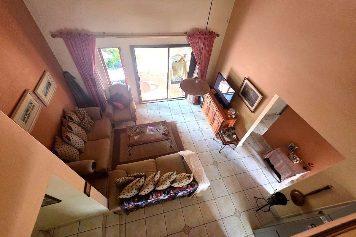 A high-ceilinged living room featuring tiled flooring and a large sliding glass door providing access to the outdoor patio area.