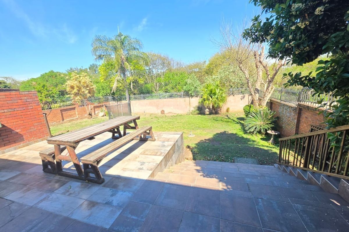 A spacious rear garden featuring a tiled patio area, brick boundary walls with security fencing, and a staircase leading to the lawn.
