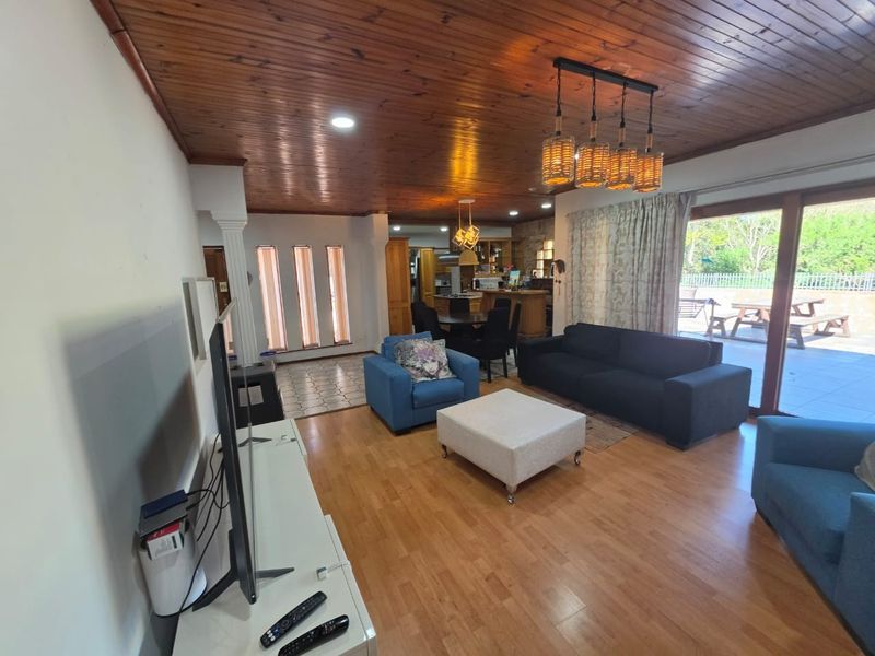 Spacious open-plan living and dining area featuring a warm timber ceiling, laminate flooring, and direct access to the outdoor patio through sliding glass doors.