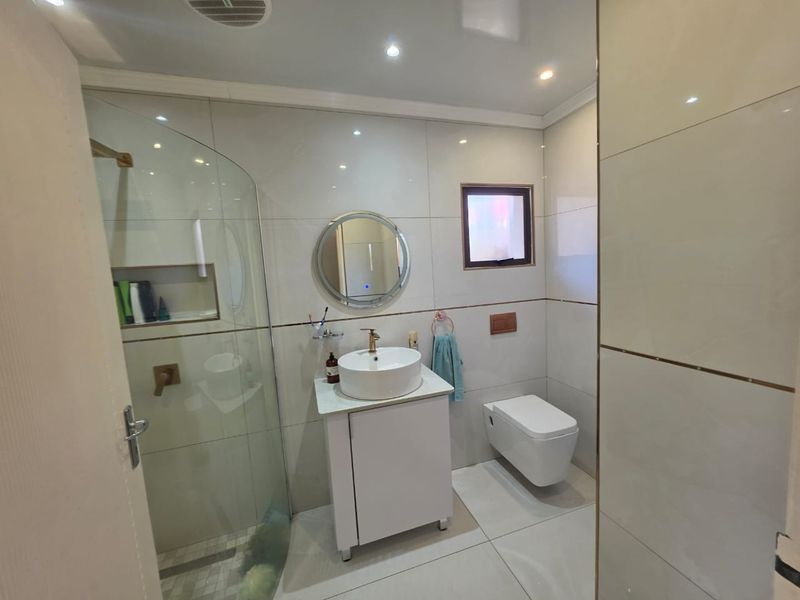 Modern bathroom featuring a wall-mounted toilet, vessel sink vanity, and a glass-enclosed shower with a built-in niche and contemporary tiled finishes.