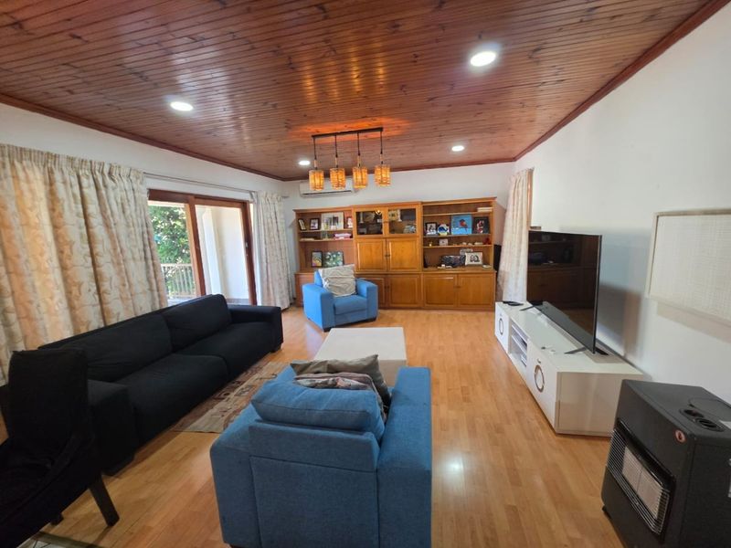 Spacious living room featuring warm timber ceilings, hardwood flooring, built-in cabinetry, and direct access to an outdoor area through sliding glass doors.