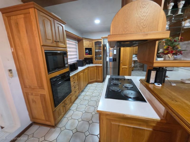 A functional kitchen featuring extensive wooden cabinetry, built-in oven, microwave, and electric hob with a tiled floor.