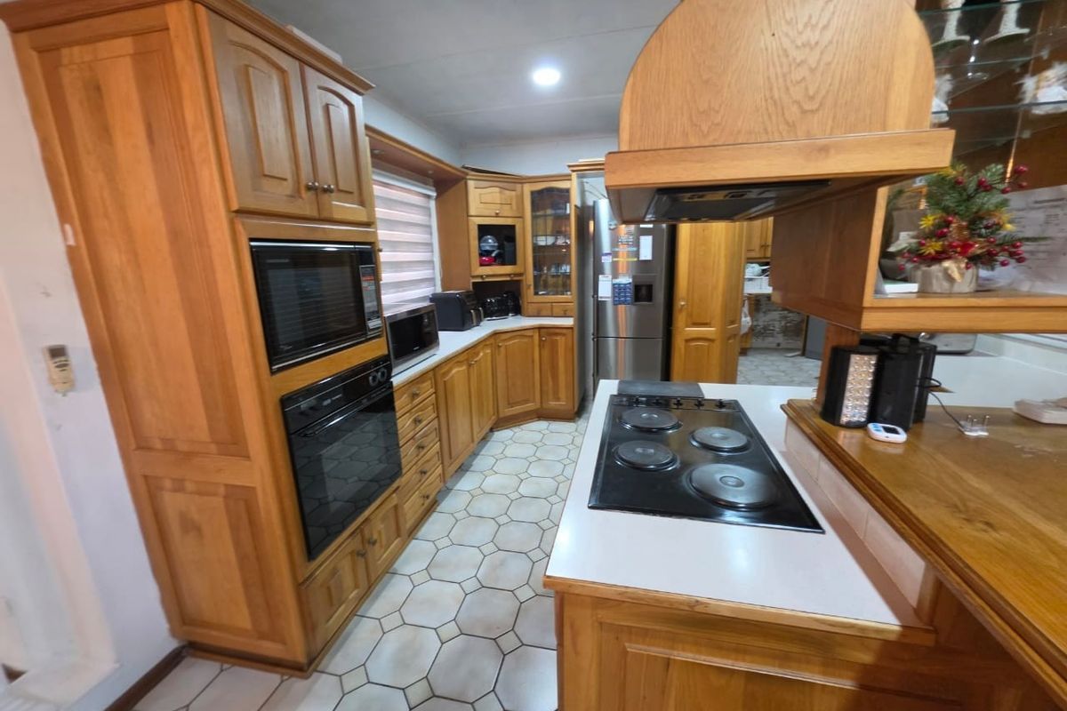 A functional kitchen featuring extensive wooden cabinetry, built-in oven, microwave, and electric hob with a tiled floor.