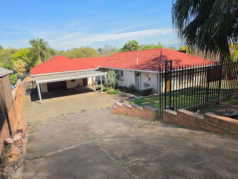 Front view of a single-story house featuring a red tiled roof, a spacious concrete driveway, a carport, and perimeter security fencing.