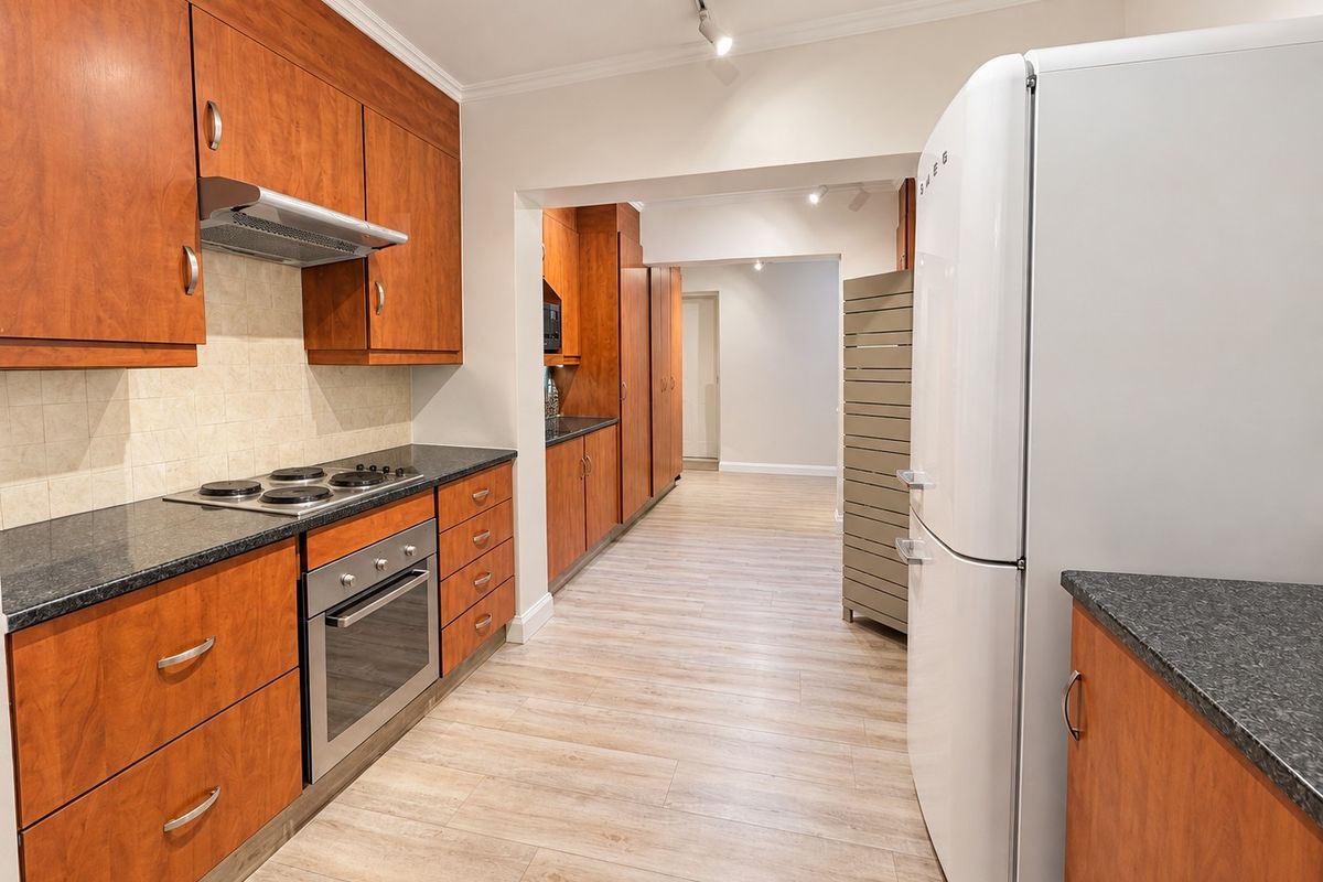 A functional kitchen featuring wood-finish cabinetry, granite countertops, integrated appliances, and light-toned laminate flooring, leading into a secondary prep or utility area.