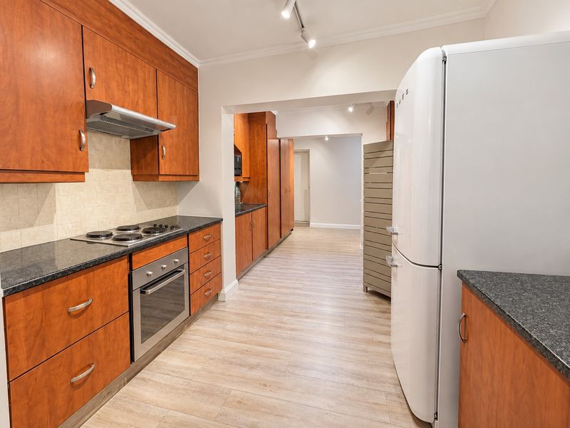 A functional kitchen featuring wood-finish cabinetry, granite countertops, integrated appliances, and light-toned laminate flooring, leading into a secondary prep or utility area.