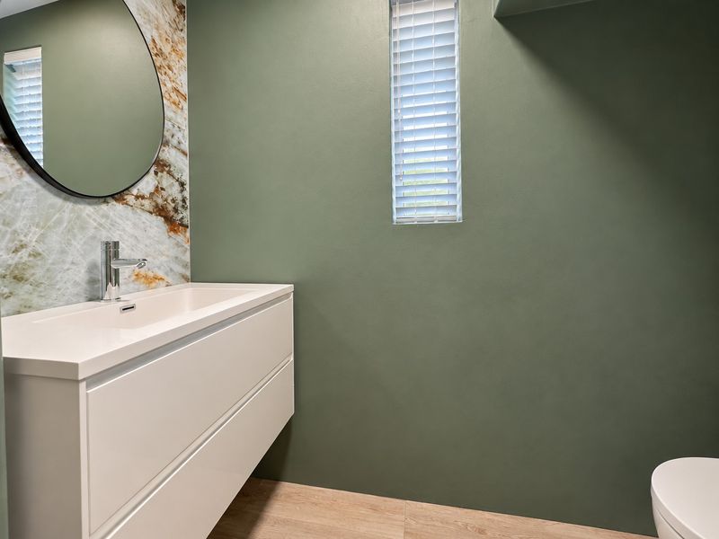 Modern bathroom featuring a wall-mounted vanity with a basin, marble-look splashback, and contemporary green wall finishes.