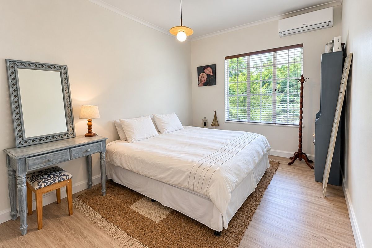 A well-maintained bedroom featuring light laminate flooring, a split-system air conditioner, and large windows with venetian blinds for natural light.