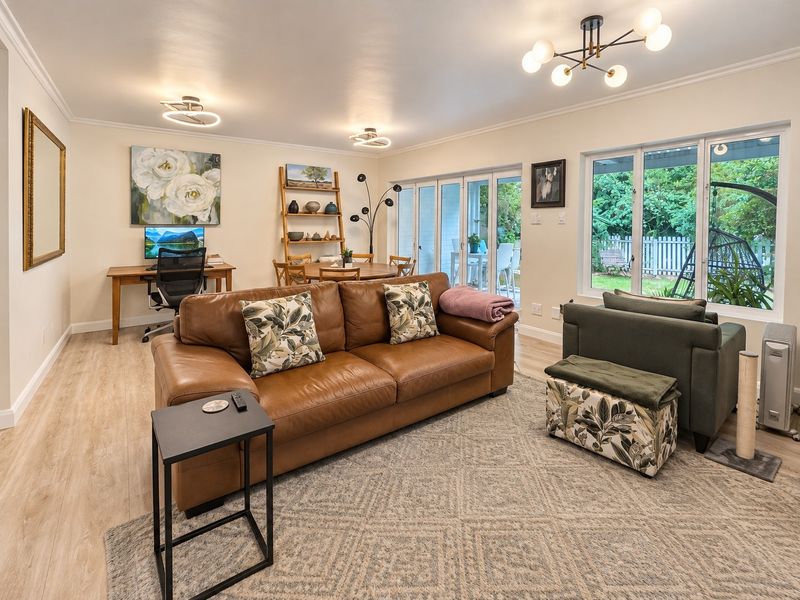 Spacious open-plan living area featuring light laminate flooring, modern lighting, and large sliding glass doors providing direct access to the rear patio and garden.