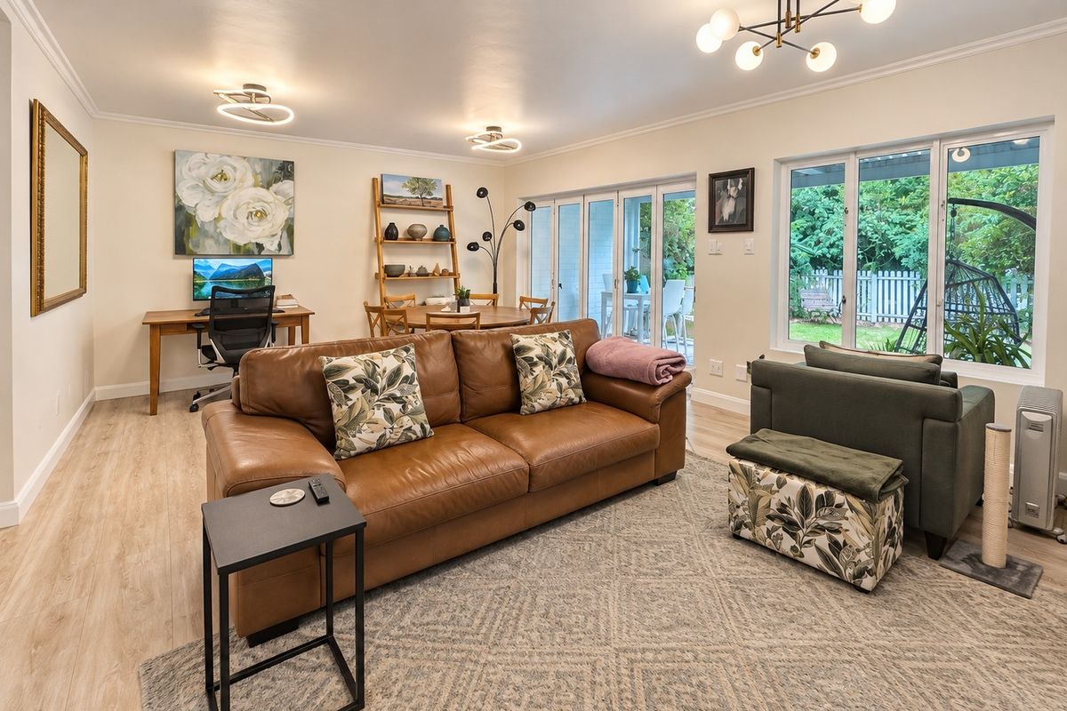 Spacious open-plan living area featuring light laminate flooring, modern lighting, and large sliding glass doors providing direct access to the rear patio and garden.