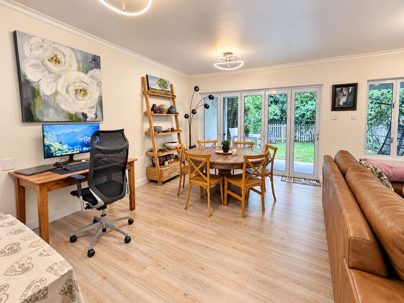 An open-plan living and dining area featuring light wood-look laminate flooring, modern bi-fold doors leading to the garden, and contemporary ceiling lighting.