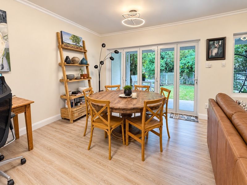 Bright open-plan dining area featuring light wood-look laminate flooring, crown molding, and bi-fold doors providing seamless access to the rear garden.