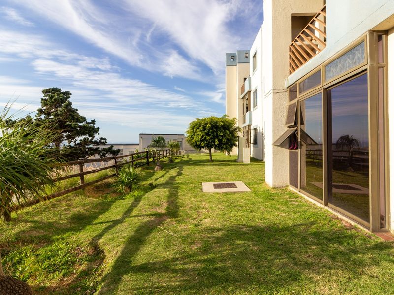 Rear exterior view of the apartment building featuring a grass lawn, timber fencing, and sliding glass doors leading to the interior.