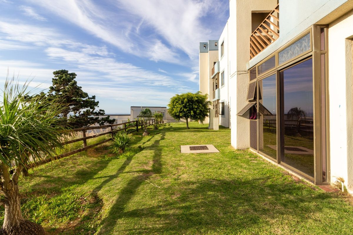 Rear exterior view of the apartment building featuring a grass lawn, timber fencing, and sliding glass doors leading to the interior.