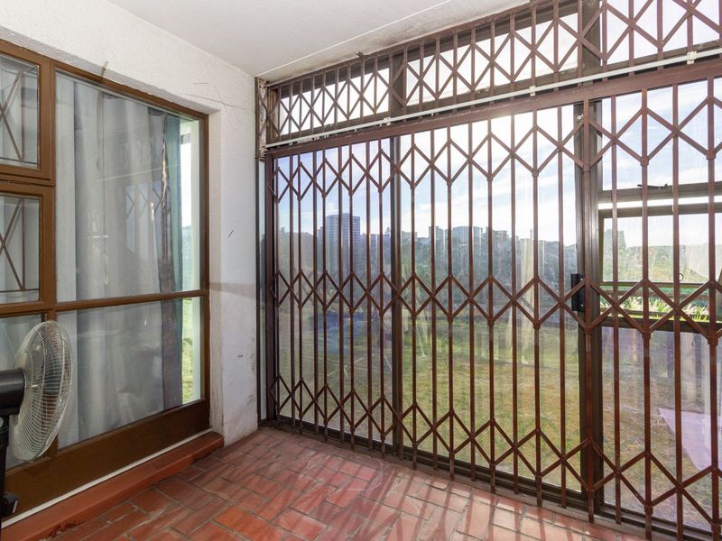 Enclosed balcony area featuring terracotta tile flooring and a metal security gate, offering a functional outdoor transition space.
