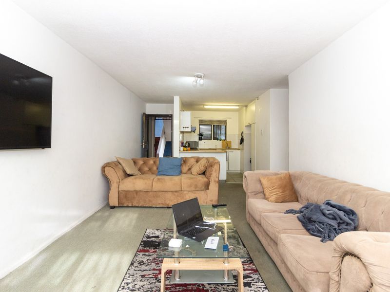 Open plan living area featuring a connected kitchen space with built-in cabinetry and sink, finished with carpet flooring throughout.