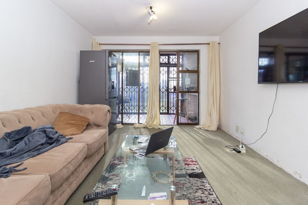 Living room featuring carpeted flooring, wall-mounted television, and sliding glass doors leading to an outdoor area with security gate.