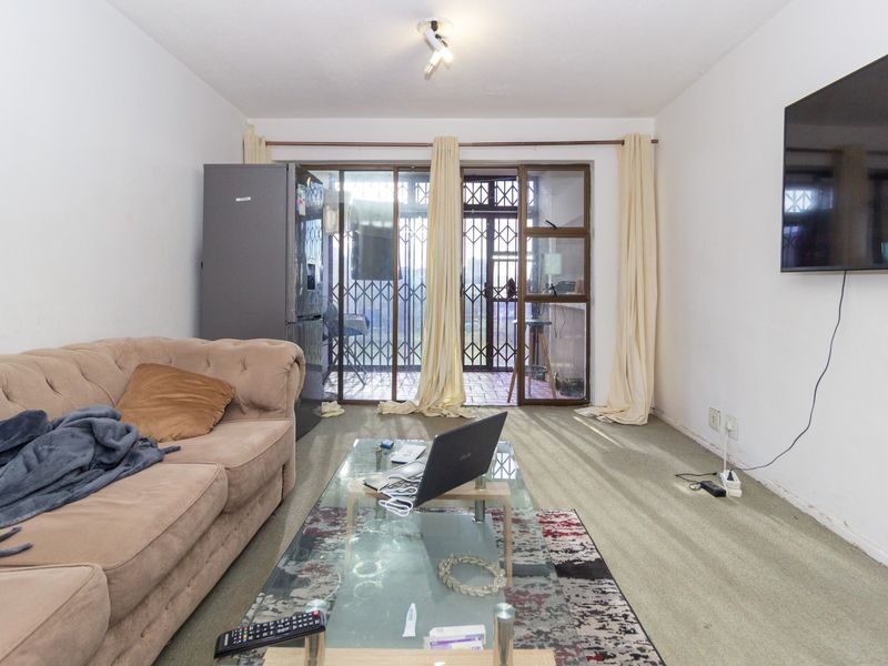 Living room featuring carpeted flooring, wall-mounted television, and sliding glass doors leading to an outdoor area with security gate.